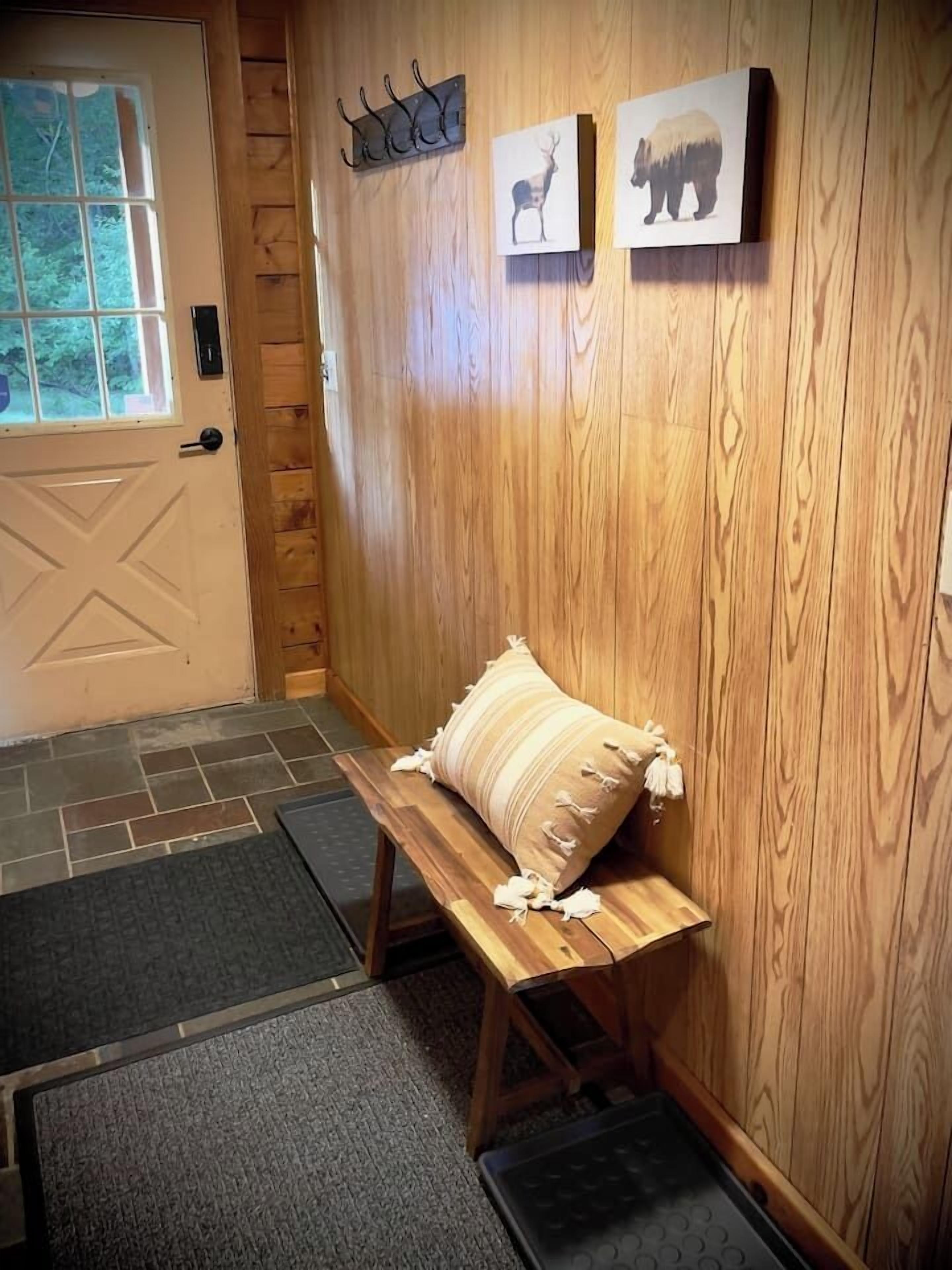 Interior de madera con un banco, una puerta y dos cuadros de animales en la pared.