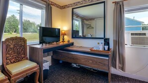 A hotel room with a wooden desk, a television, a lamp, a mirror, and a view of the outdoors. - The Green Cottage@ Twin Hills Cottages (Ellsworth)