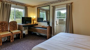 A hotel room with a bed, a desk with a TV, two chairs, and a window with curtains. - The Green Cottage@ Twin Hills Cottages (Ellsworth)