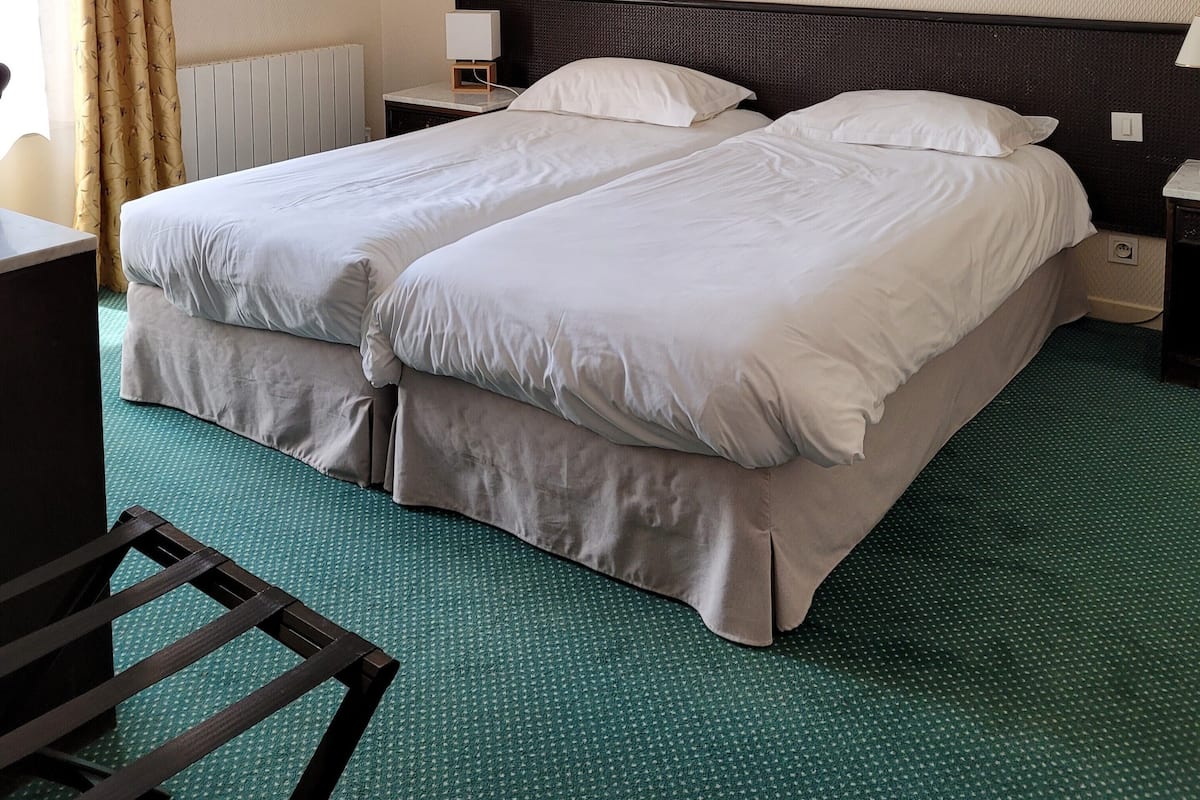 A hotel room with two beds, a nightstand, an air conditioning unit, a framed picture on the wall, and a desk with a chair.