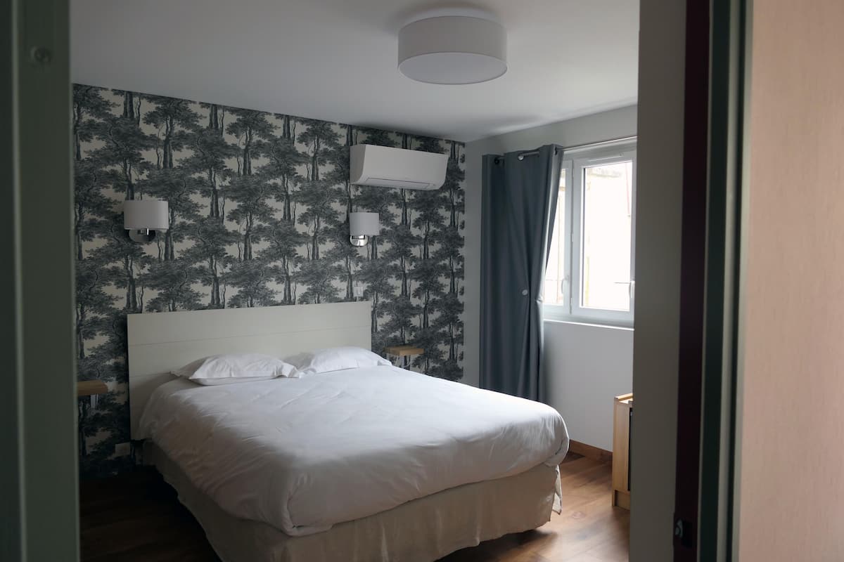 A bedroom with a bed, two wall-mounted lights, an air conditioner, a window with curtains, and a door.