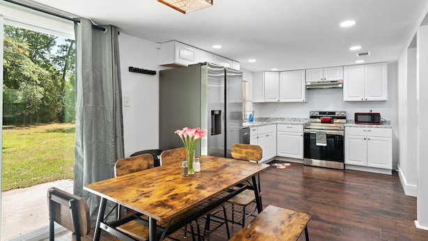 A modern kitchen with white cabinets, a wooden dining table, and a view of the outdoors. - NEW! 19 Minutes from Savannah Historic District (Bloomingdale)