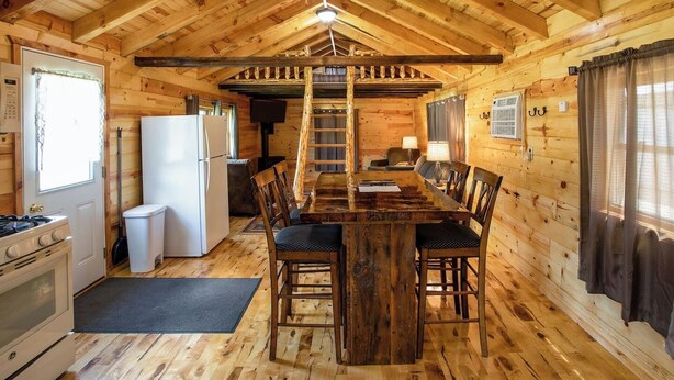 L’intérieur d’une cabane en bois comprend une table à manger, des chaises, un réfrigérateur, une cuisinière et une échelle menant à une mezzanine.