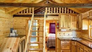 L’intérieur d’une cabane en bois comprend une chambre à coucher située en mezzanine, une cuisine avec des meubles en bois et un escalier.