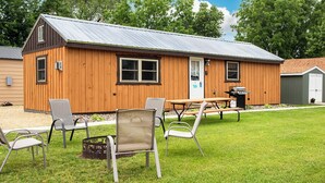 Une cabane en bois avec un toit en métal, une table de pique-nique et quatre chaises.