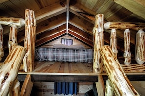 Un dormitorio estilo loft con techo inclinado, vigas de madera, cama con manta escocesa y ventana con cortinas.