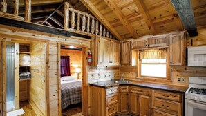 L'intérieur d'une cabane en bois, avec un lit, un coin cuisine et une fenêtre.