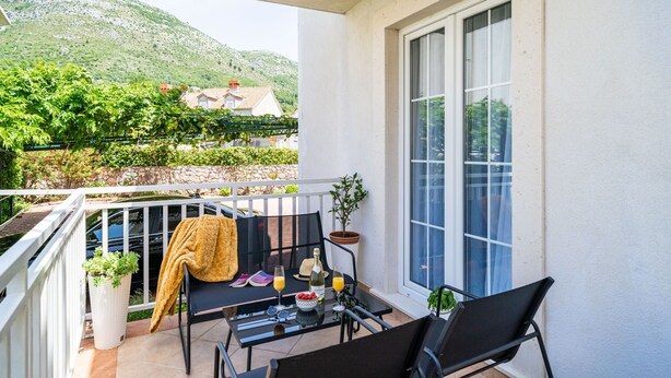 Een balkon met een tafel voor twee personen, een bloempot en een uitzicht op een berg en huizen op de achtergrond.