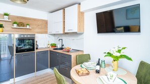 Een moderne keuken met een inbouwoven, een eethoek met een ronde tafel en stoelen, en een televisie die aan de muur is bevestigd.