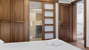Une chambre d’hôtel avec un grand lit, une armoire en bois et une salle de bain visible à travers une porte en verre.