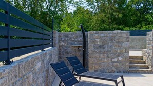 Un espace extérieur ensoleillé, aménagé avec deux fauteuils et un mur en pierre.