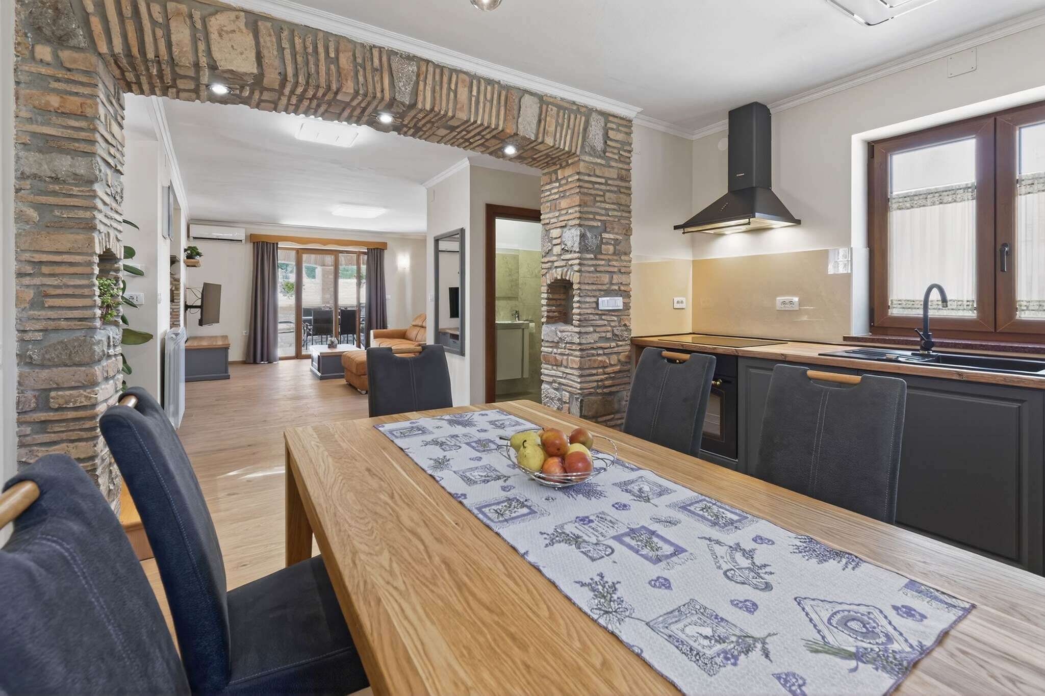 A modern kitchen with a stone archway, a dining area with a table set for two, and a view into the living room.