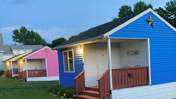 A row of small, colorful cabins with wooden steps leading to the entrance, set on a grassy area. - The Blue Cottage@ Twin Hills Cottages (Ellsworth)