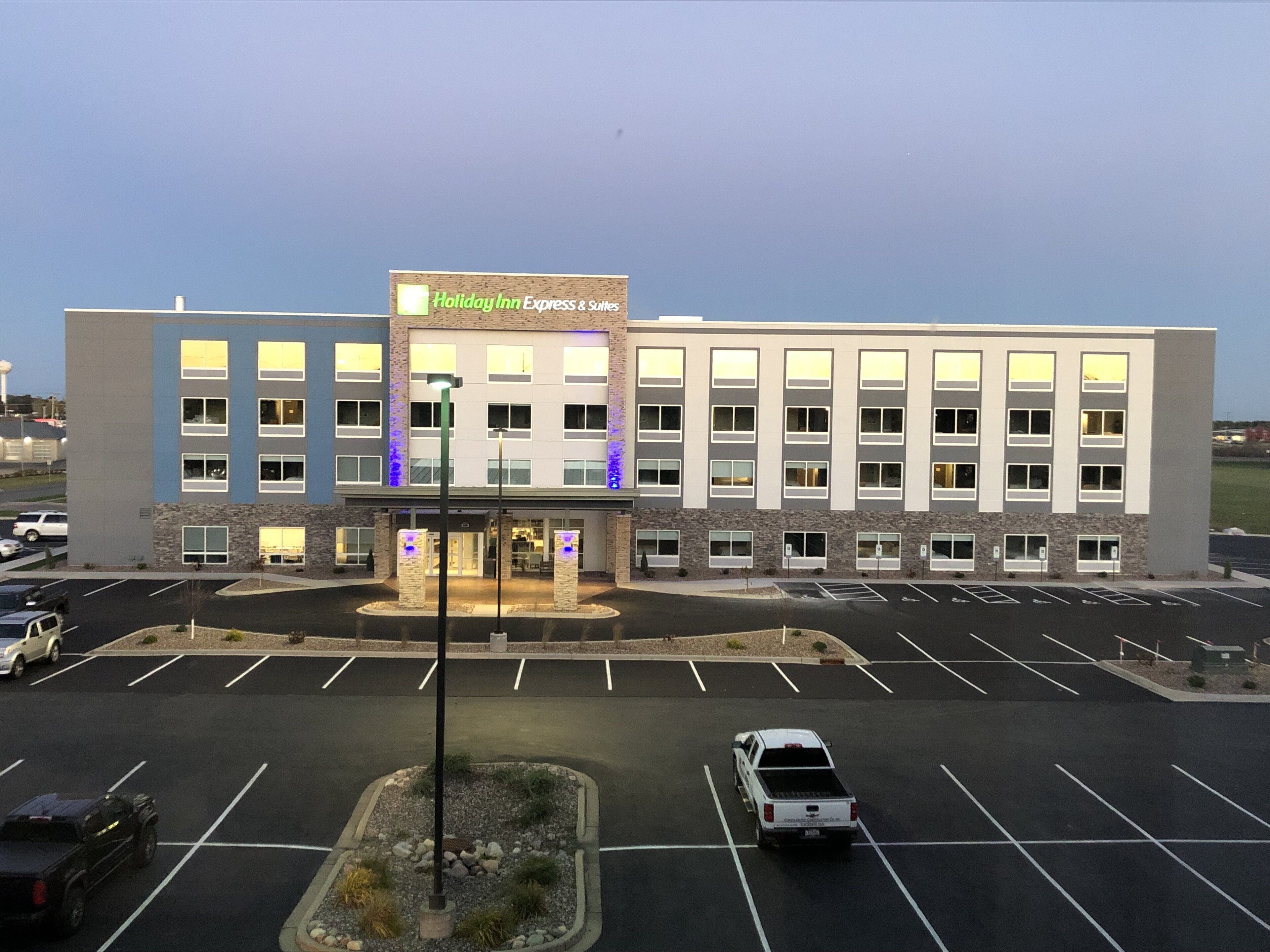 Ein Holiday Inn Express & Suites Gebäude mit Parkplatz und einigen Fahrzeugen.
