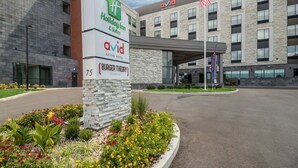A Holiday Inn & Suites building with a brick facade, a sign for Burger Theory restaurant, and a landscaped entrance area.