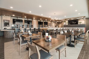 Un restaurante moderno con mesas y sillas de madera, una zona de bar y una pantalla grande.