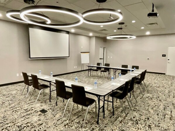 Un salón de conferencias con una larga mesa, sillas, una pantalla de proyector y una pizarra.