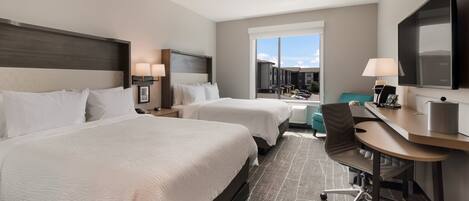 A hotel room with two beds, a desk, a chair, a TV, and a window with a view of the outside.