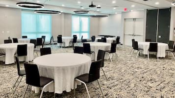 A conference room with round tables and chairs, large windows, and a carpeted floor.