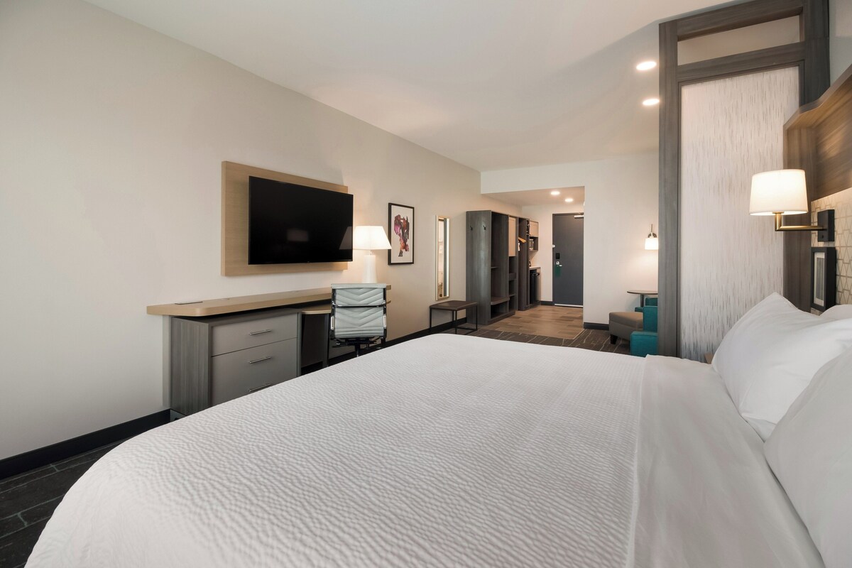 Une chambre d’hôtel avec un grand lit, un bureau avec une chaise, un téléviseur à écran plat fixé au mur et une petite table avec une lampe.