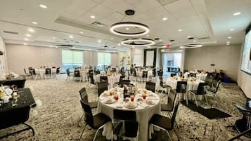 Un amplio salón de banquetes con mesas redondas dispuestas para comer, piso alfombrado y un alto techo con iluminación empotrada.