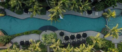 An aerial view of a resort with a swimming pool, palm trees, and outdoor seating areas.