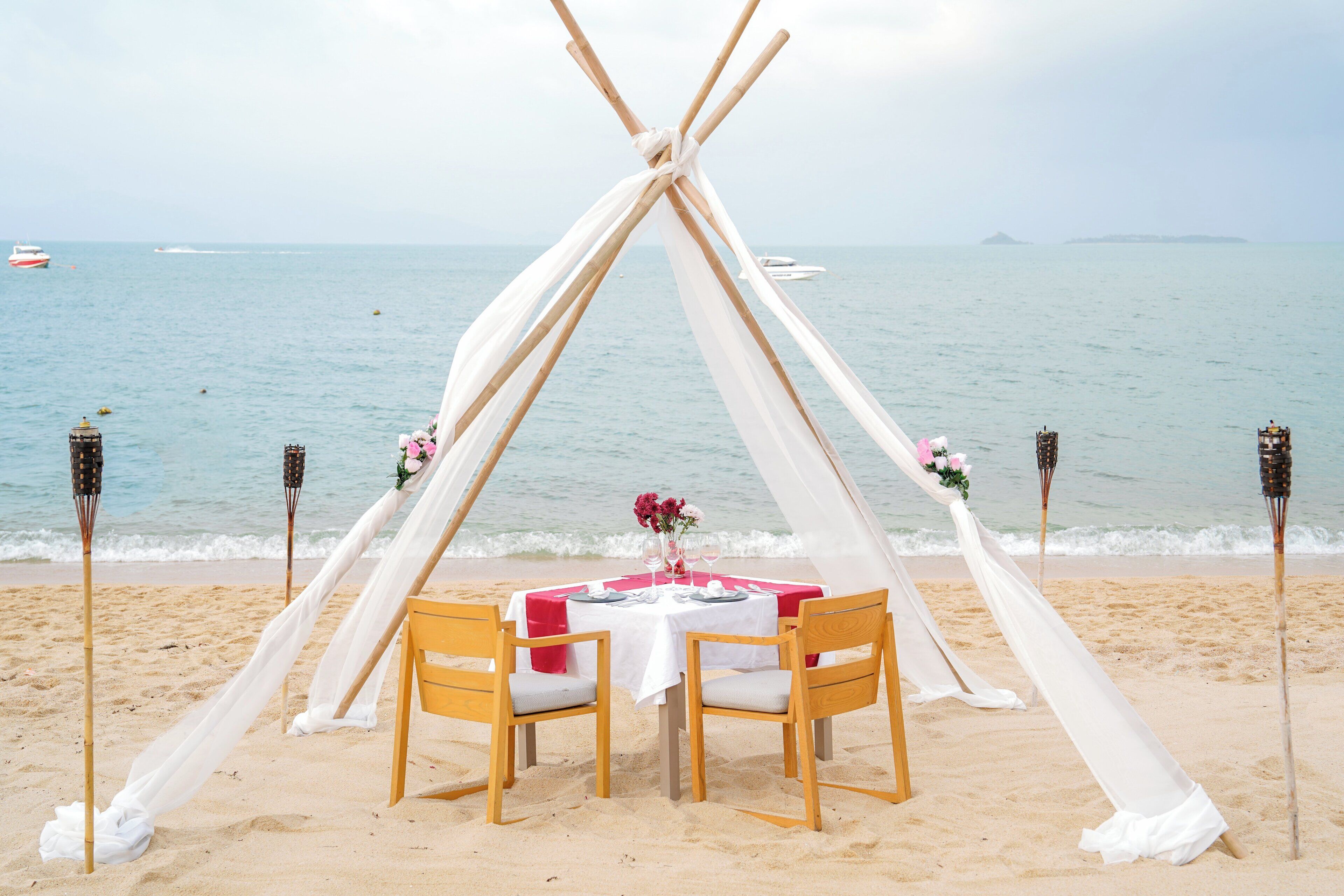 A beach wedding setup with a teepee tent, a round table, and chairs.