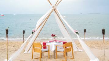 A beach wedding setup with a teepee tent, a round table, and chairs.