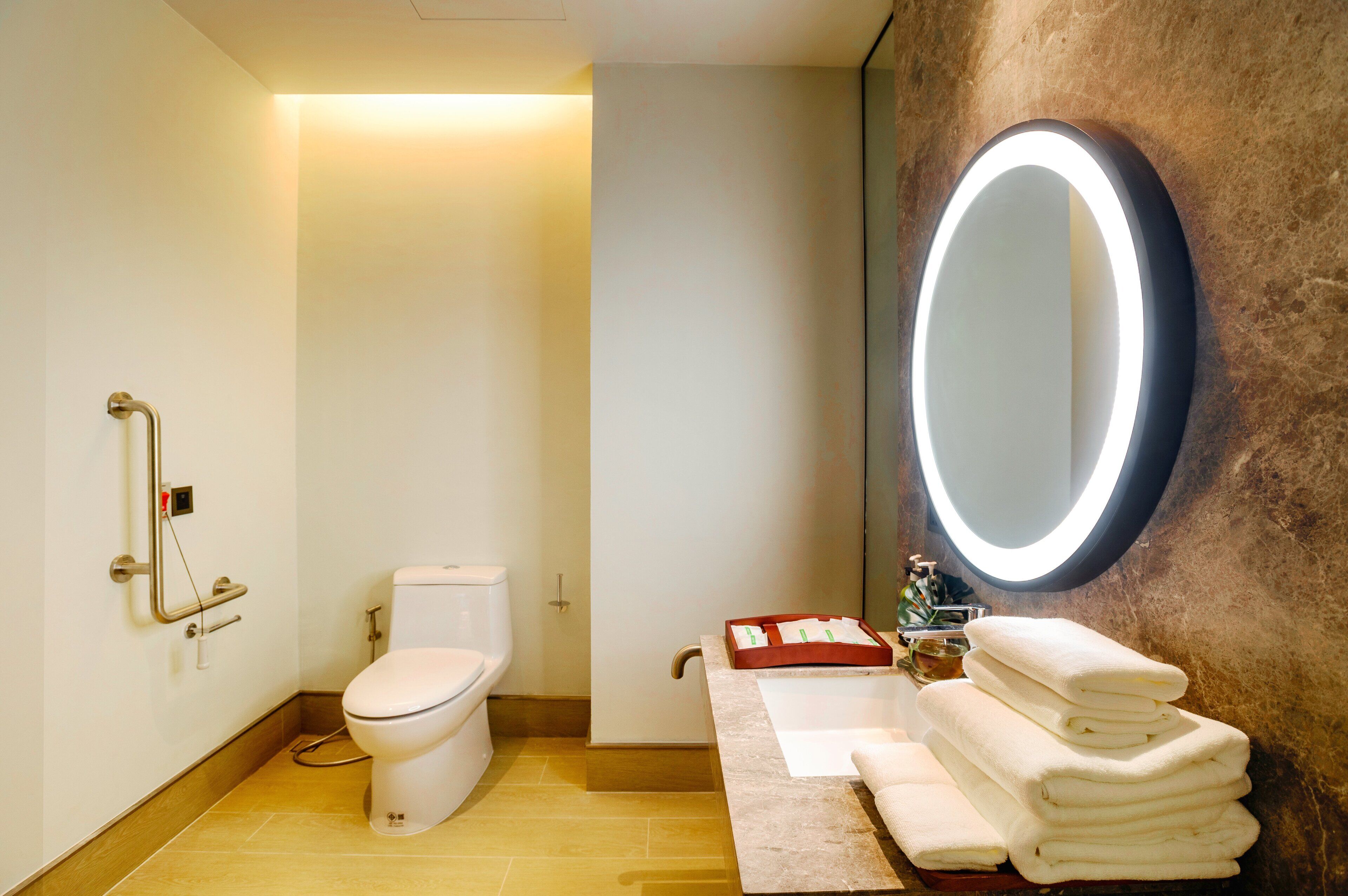 A modern bathroom with a toilet, a sink with a mirror, and a stack of towels.