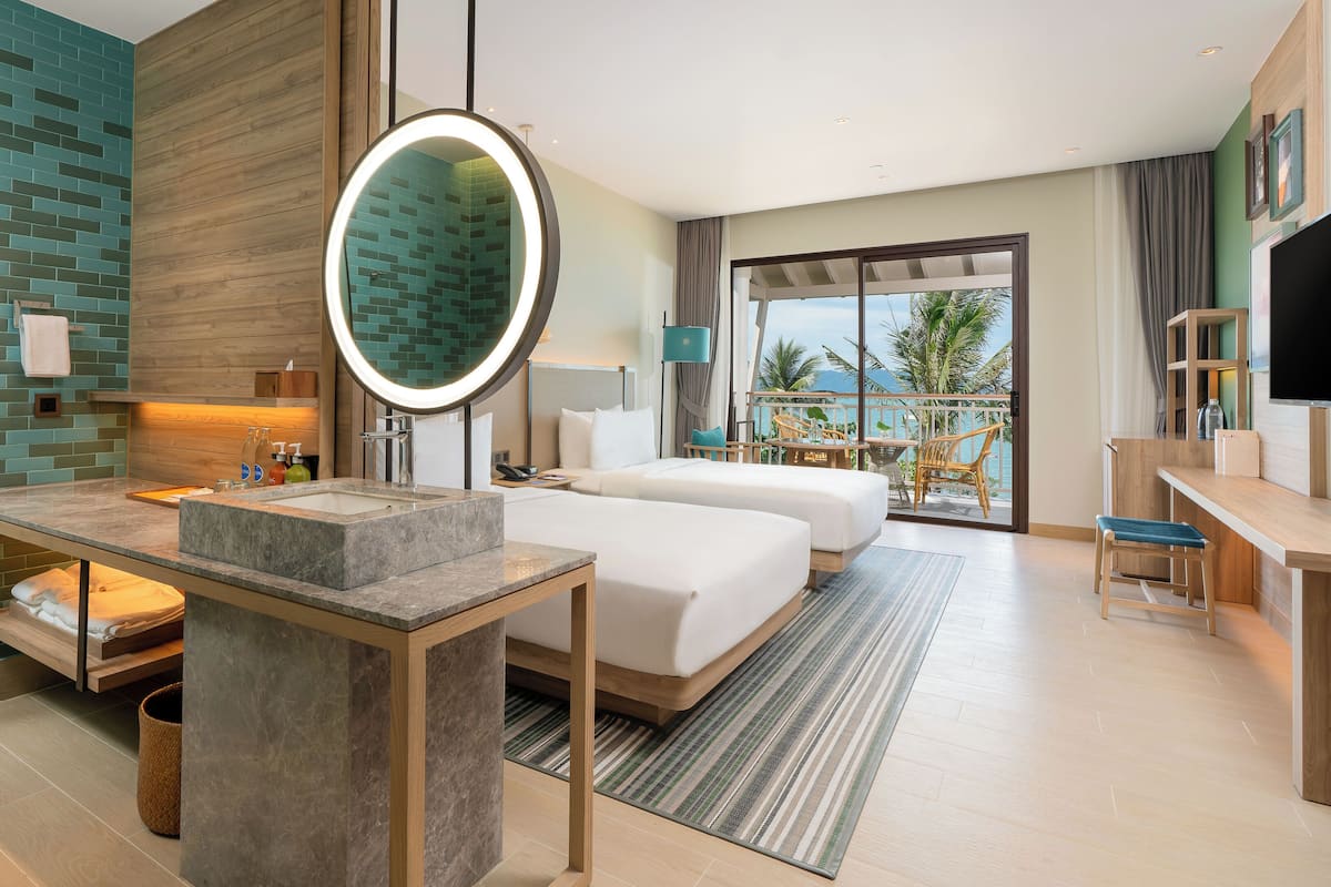 A modern hotel room with a large bed, a desk, a bathroom with a mirror, and a balcony with a view.