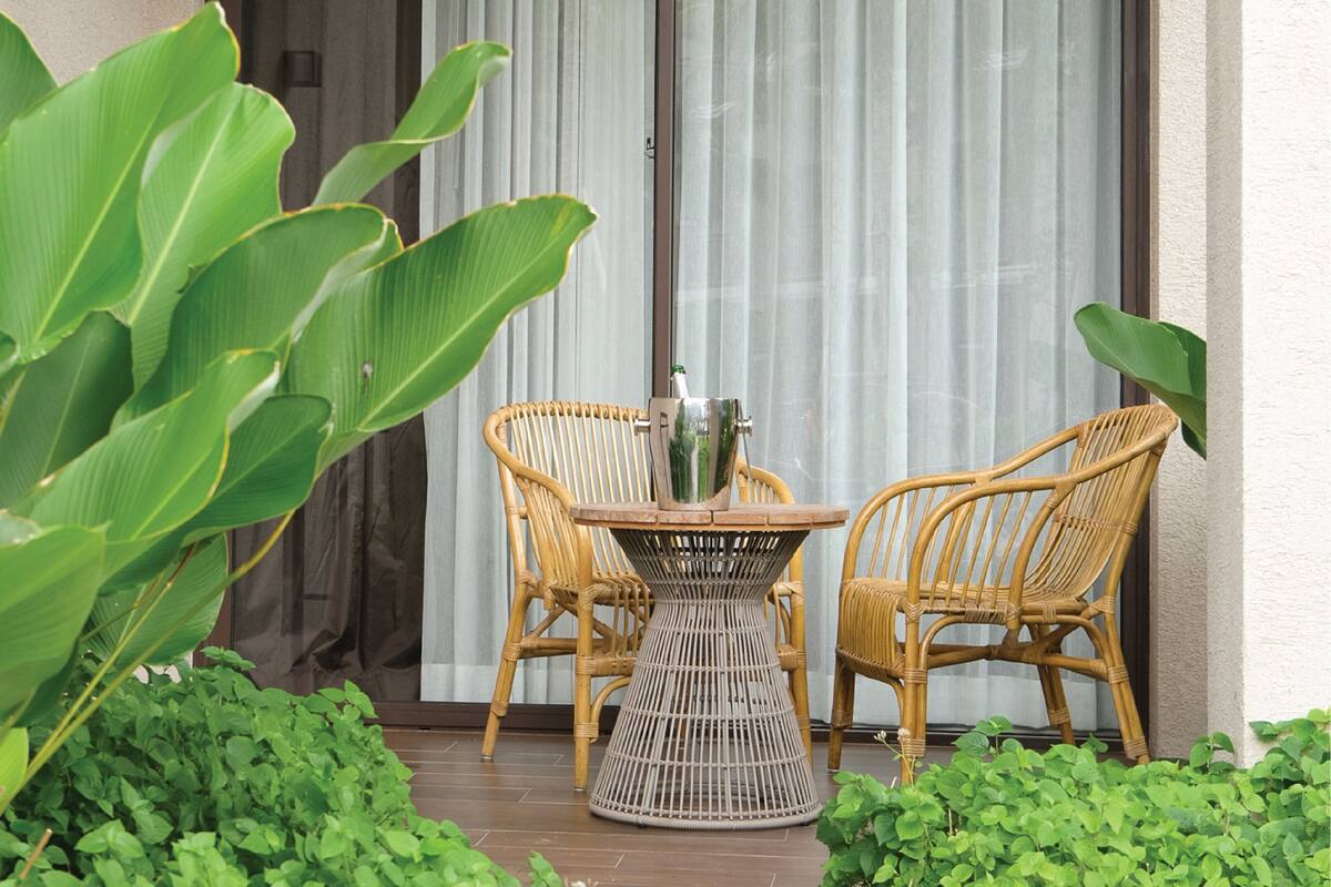 A wicker table and chairs set on a patio with large green plants.