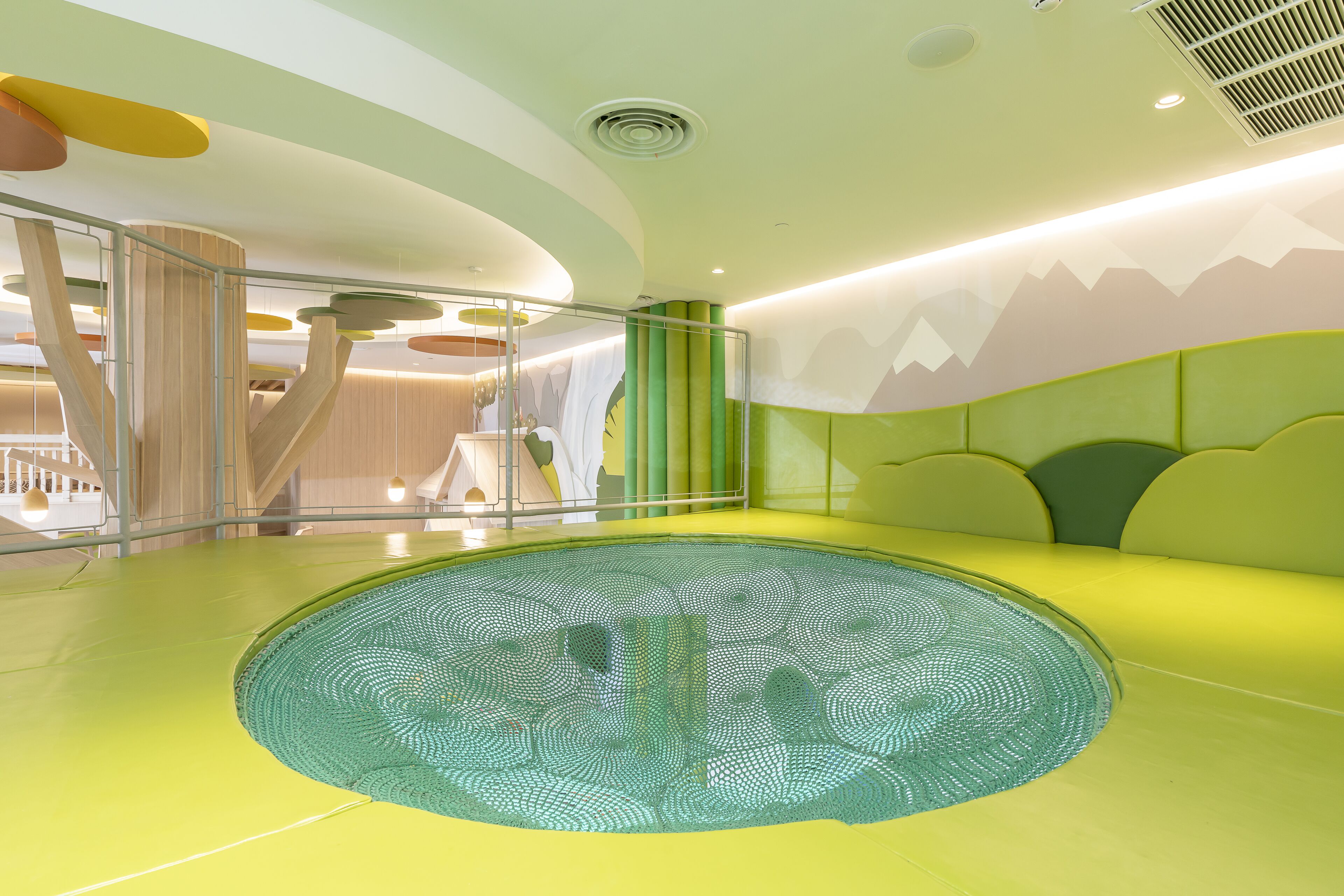 A modern indoor pool area with a unique circular design, a seating area with green and yellow cushions, and a ceiling with a mountain mural.