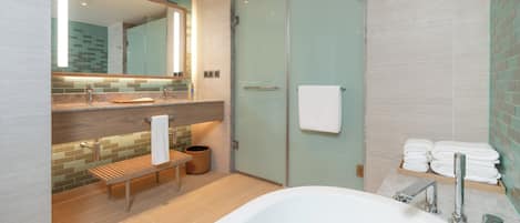 Une salle de bain moderne avec une douche à l’italienne en verre, un banc en bois, une grande baignoire et un miroir au-dessus du lavabo.