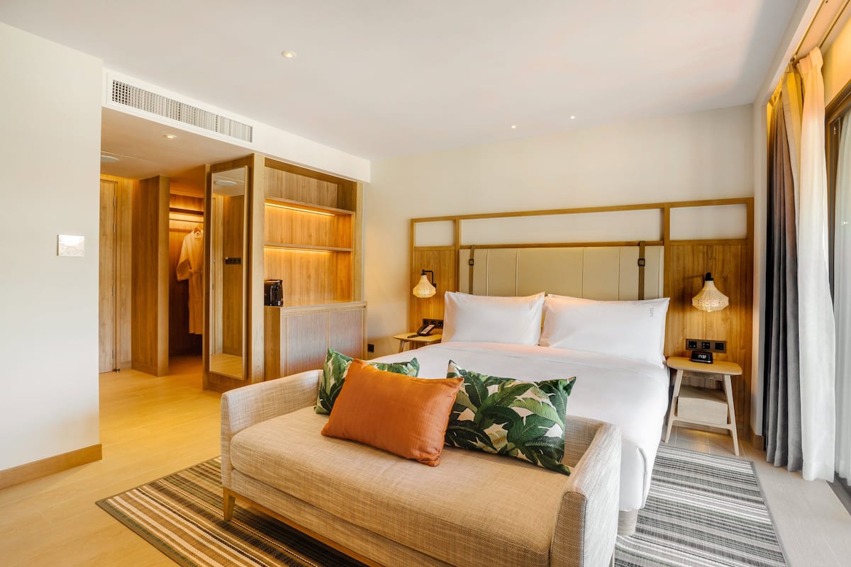 A hotel room with a bed, a sofa, a nightstand, and a walk-in closet.