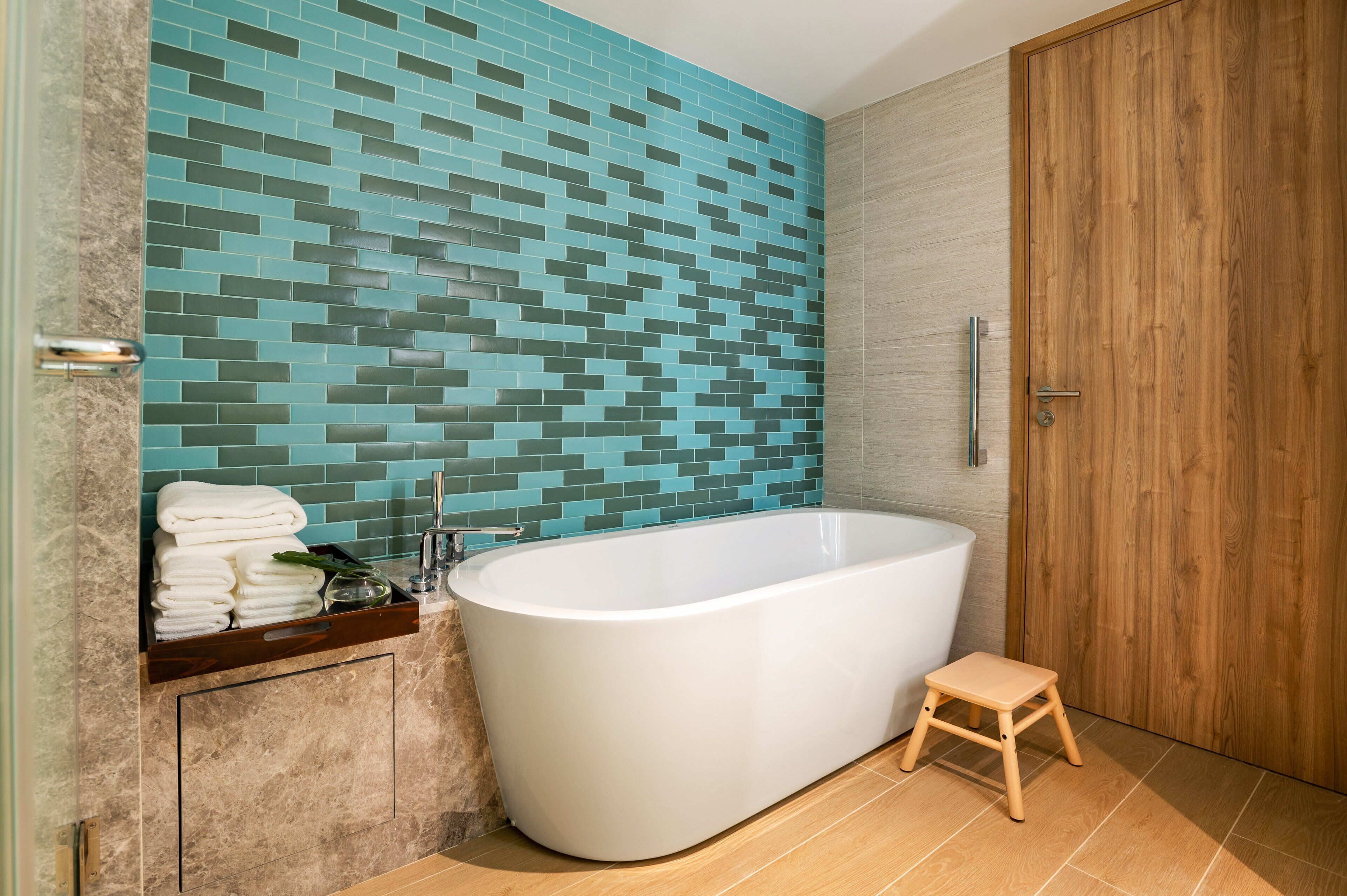 A modern bathroom with a freestanding bathtub, a wooden door, and a tiled wall.
