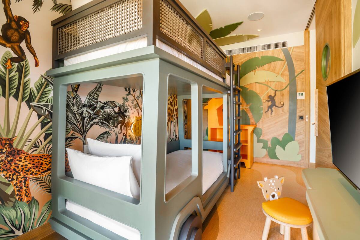 A children's room with bunk beds, a TV, and jungle-themed wall art.
