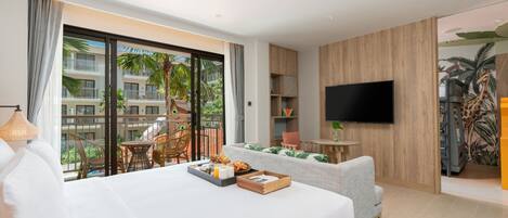 Een moderne hotelkamer met een groot bed, een televisie, een balkon met tuinmeubilair en uitzicht op een gebouw met palmbomen.