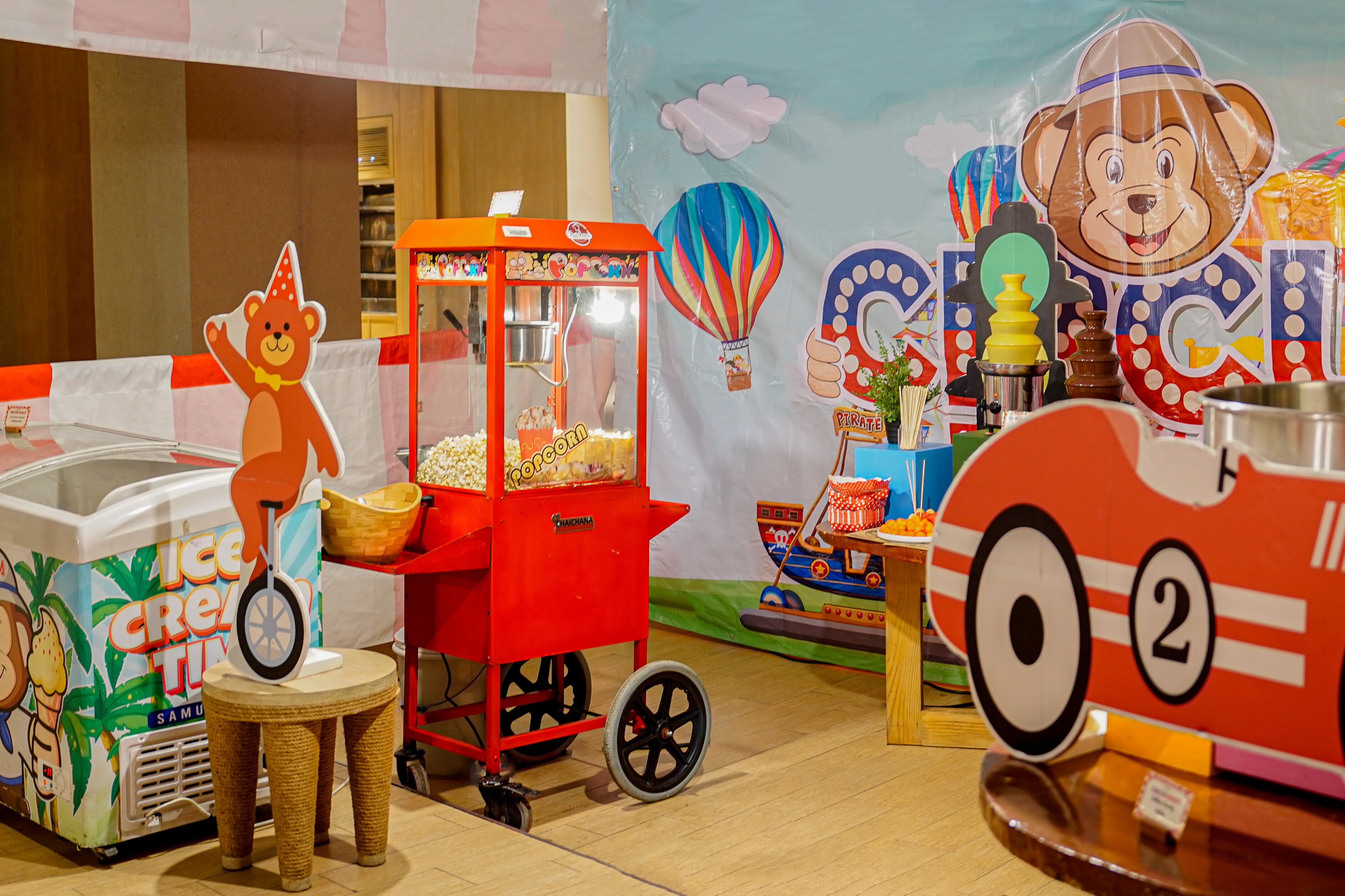 Un área de juegos infantiles con un carrito de helados con forma de oso, una decoración de globo aerostático y un tren de juguete.