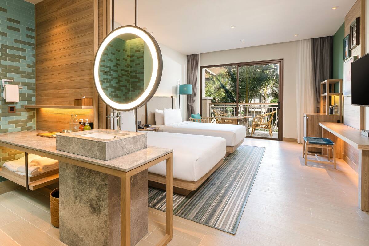 A modern hotel room with a marble bathroom, a large bed, a desk, and a balcony with a view of the outdoors.