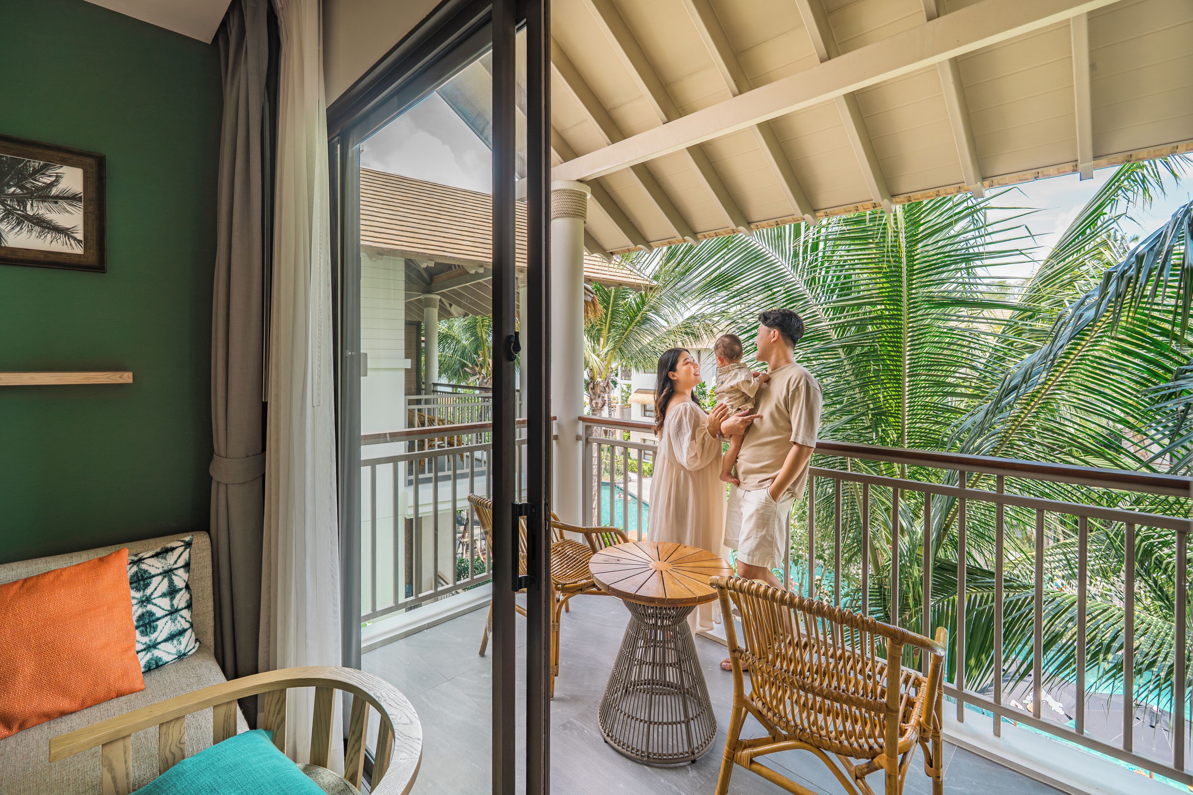 A balcony with wicker furniture, a glass door leading outside, and a view of palm trees.