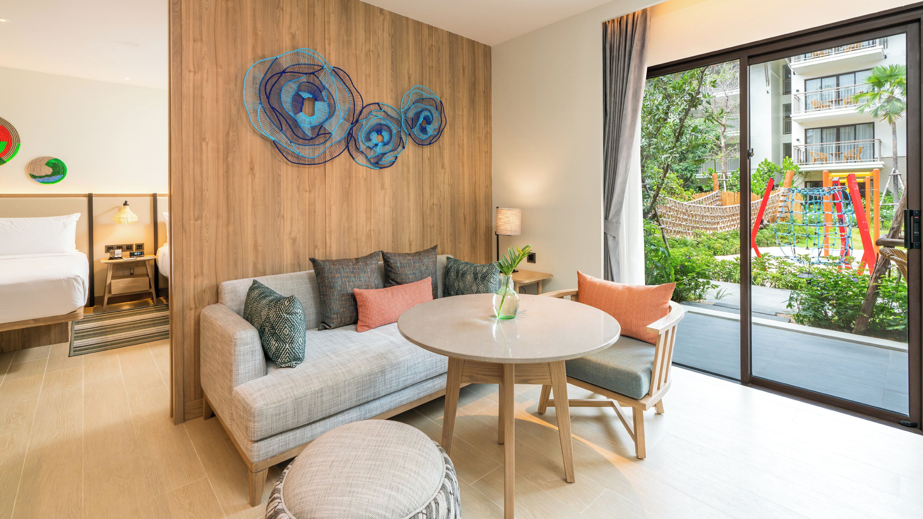 Une chambre d’hôtel moderne, dotée d’un canapé, d’une table ronde et offrant une vue sur l’aire de jeux extérieure.