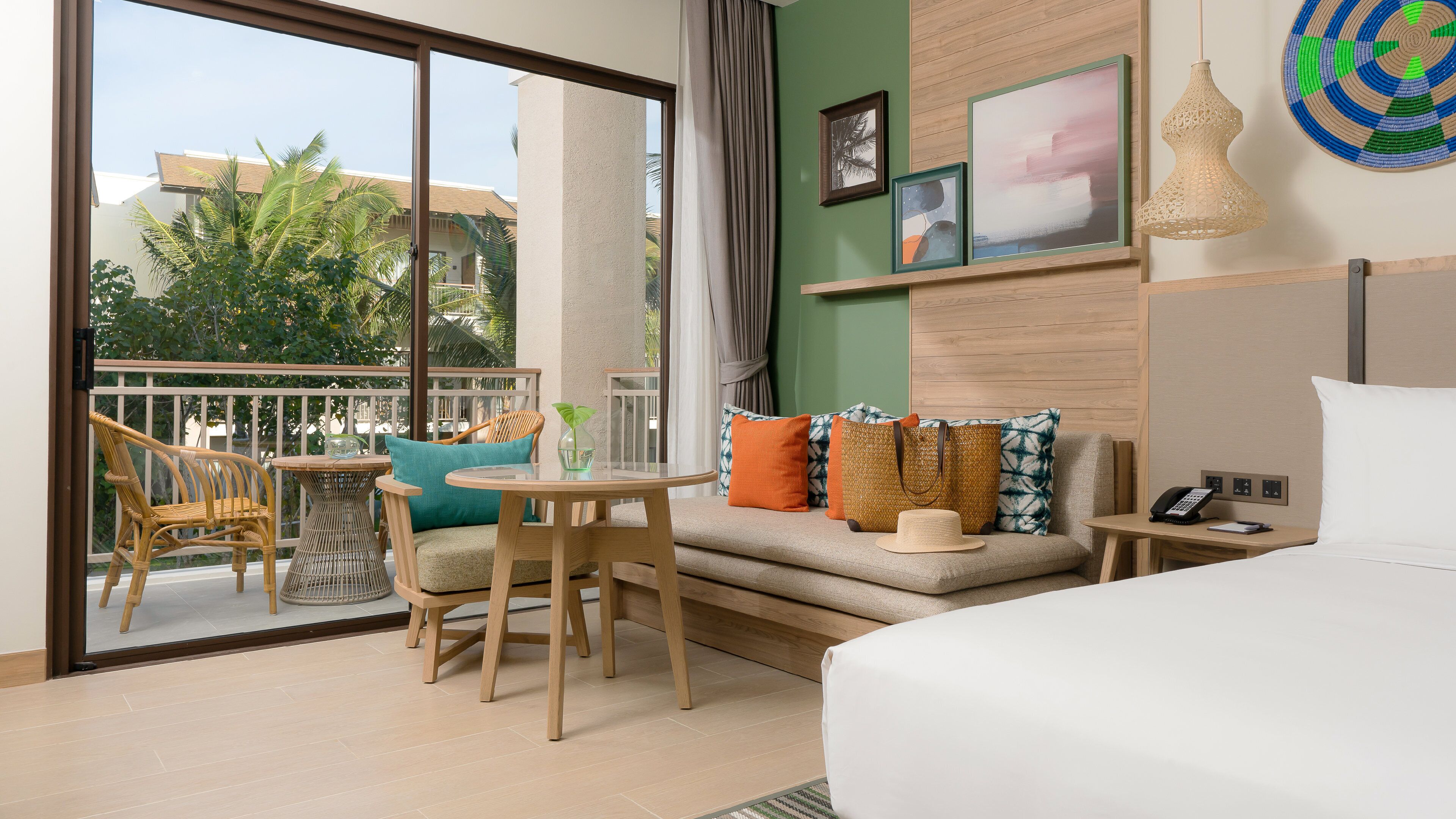 A hotel room with a balcony, a bed, a small table with chairs, and a sofa with cushions.