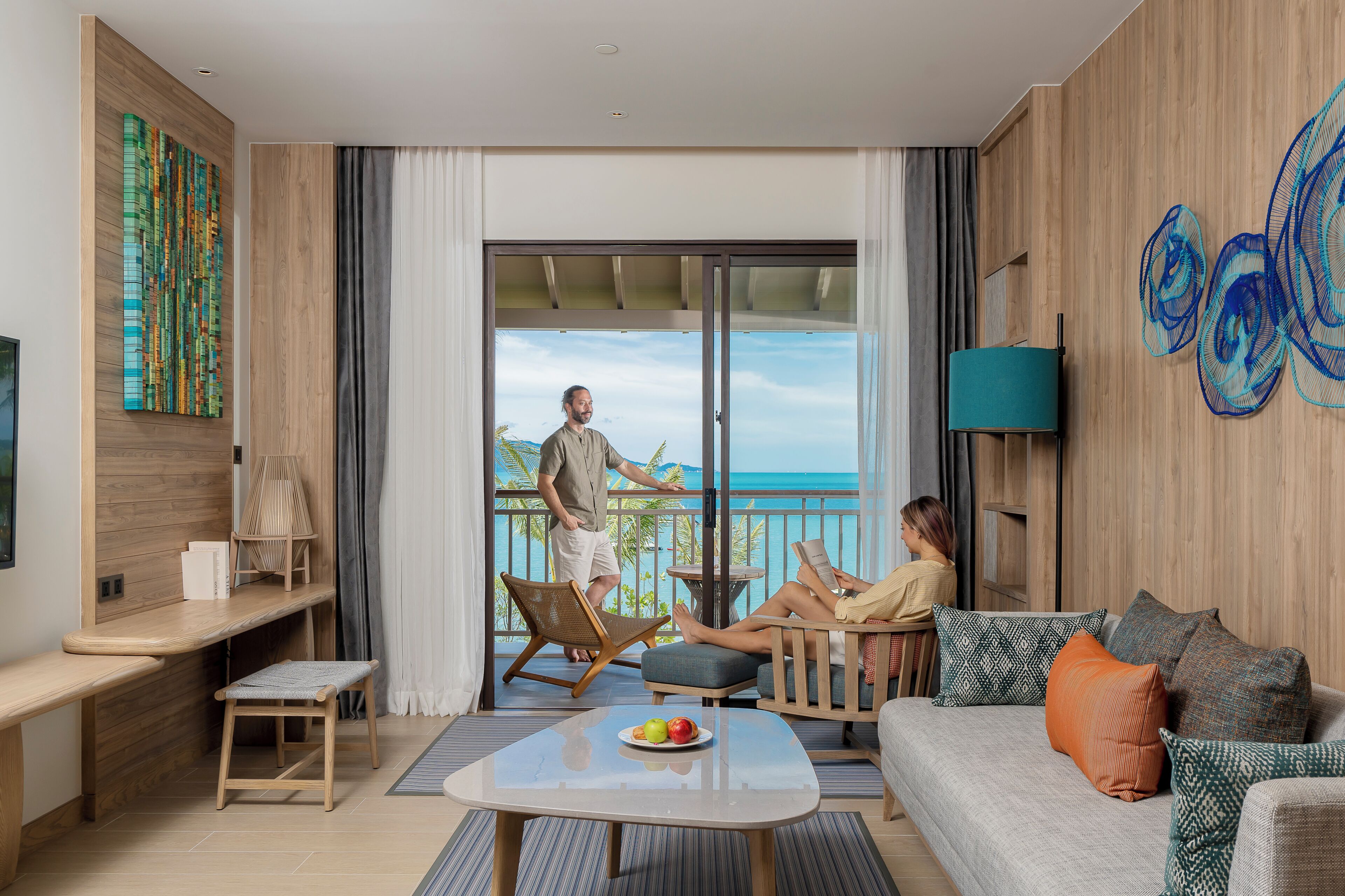 A modern hotel room with a balcony, a sofa, a coffee table, and a TV.