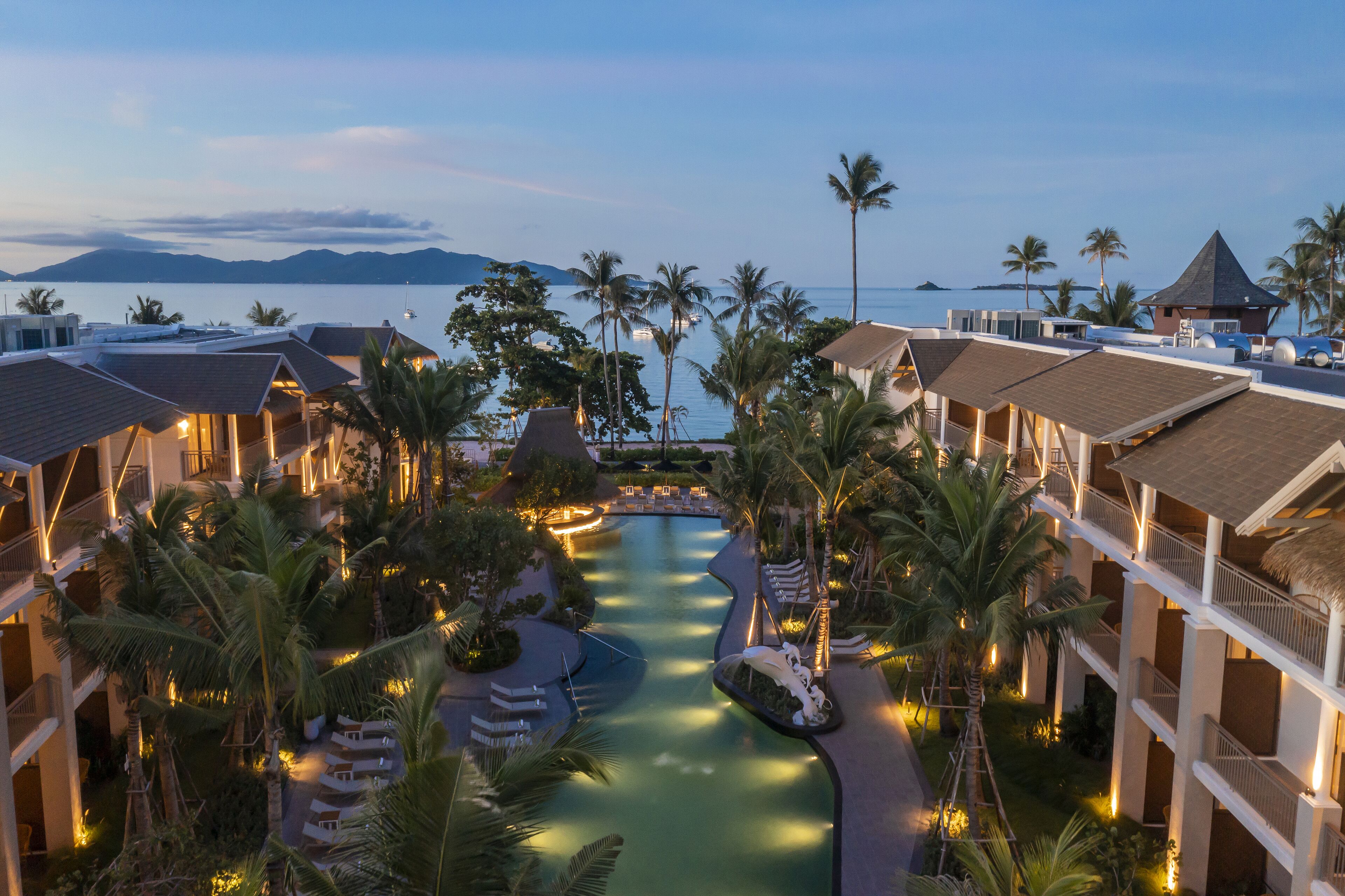 Un resort con varias edificaciones, un elemento acuático central y palmeras.