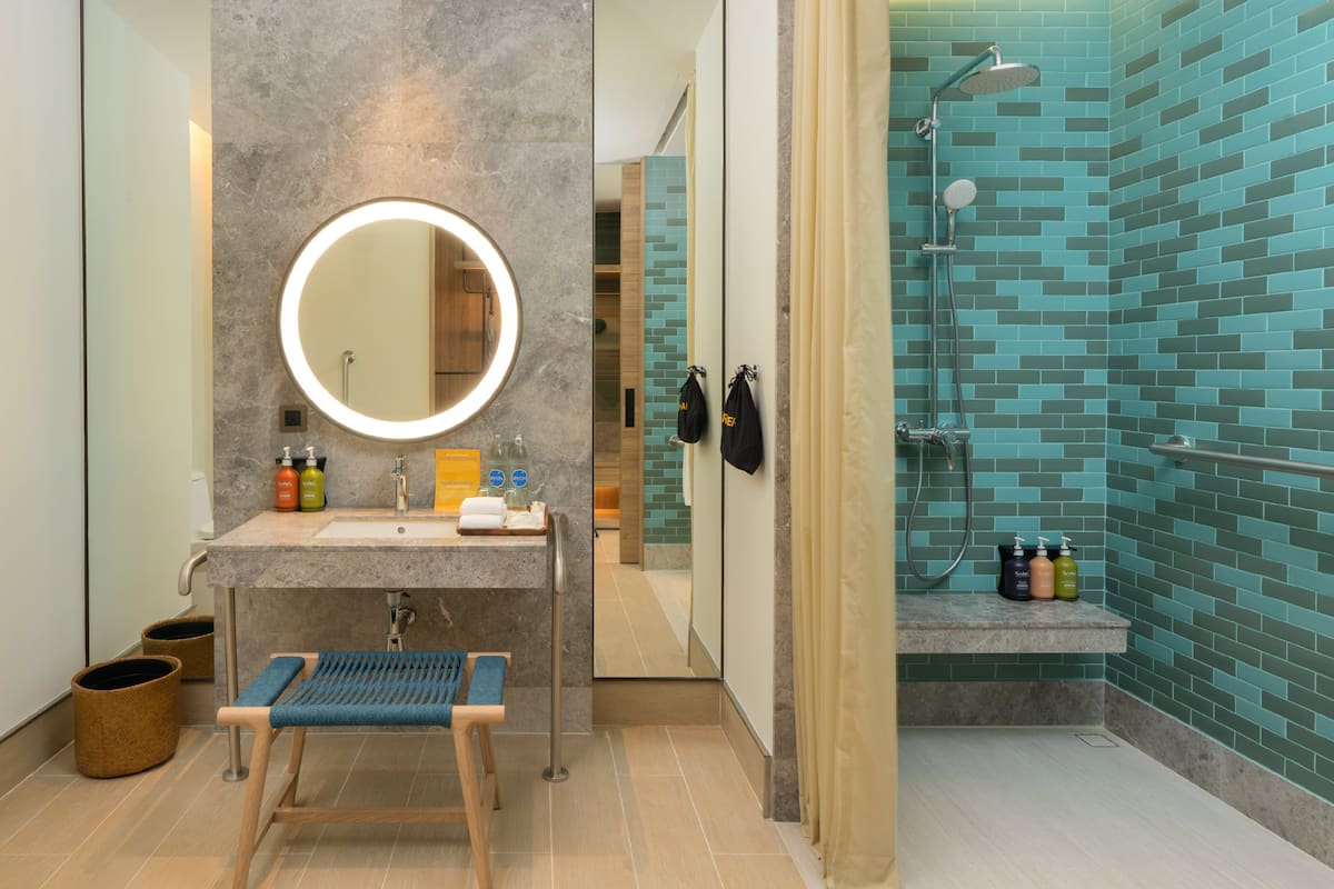 A modern bathroom with a marble vanity, a round mirror, and a shower area with blue-tiled walls.