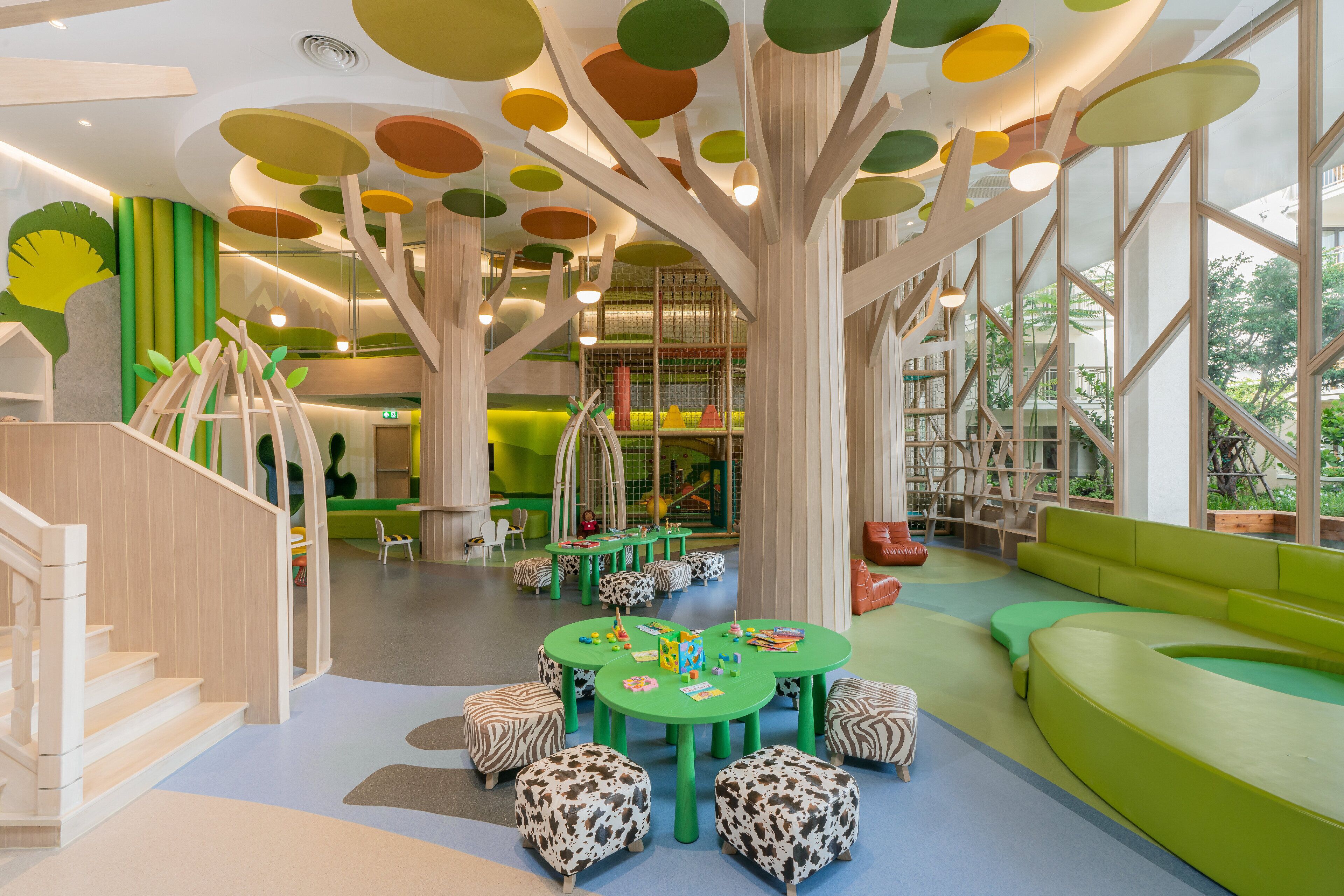 A children's play area with green tables, zebra-patterned ottomans, and a large tree-like structure with hanging lights.