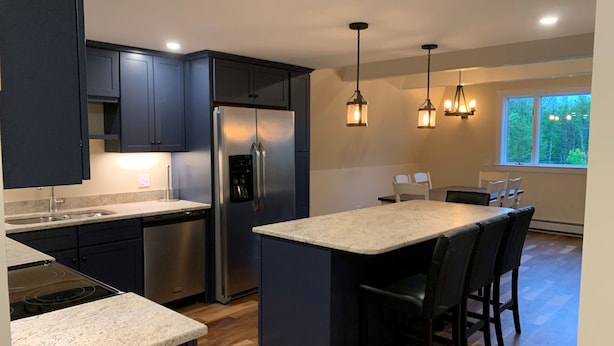 A modern kitchen with dark cabinets, stainless steel appliances, and a central island with bar stools.