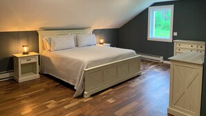 A bedroom with a bed, nightstands, a dresser, and a window with a view of greenery.