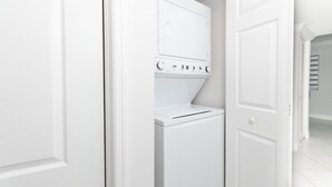 A laundry room with a front-loading washer and dryer, white walls, and a door leading to another room. - Beautiful 2/2.5 Condo w/Free Parking Fast WIFI (Miami)