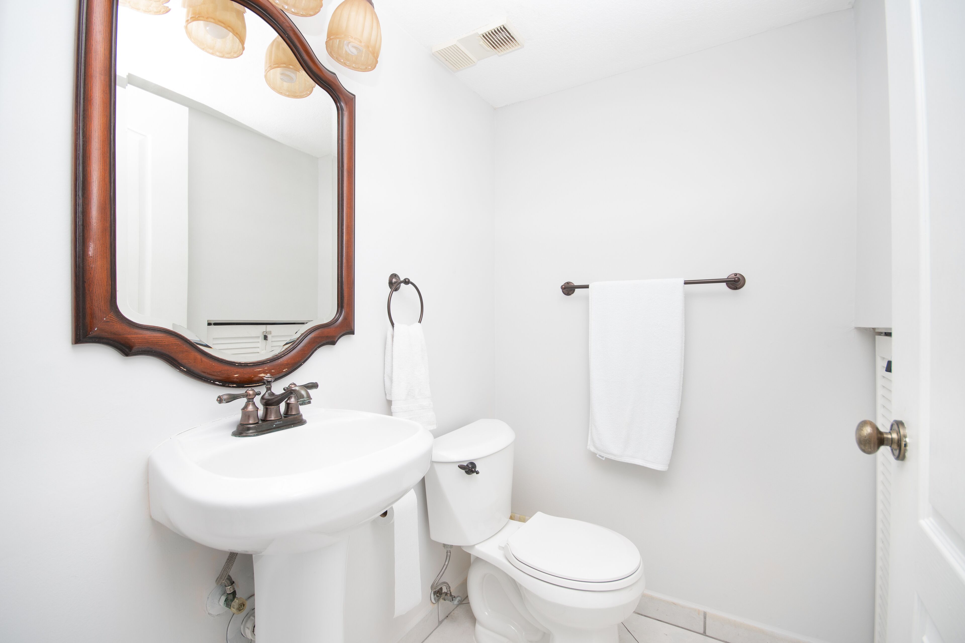 A bathroom with a white sink, a toilet, a towel rack, and a mirror with a wooden frame.